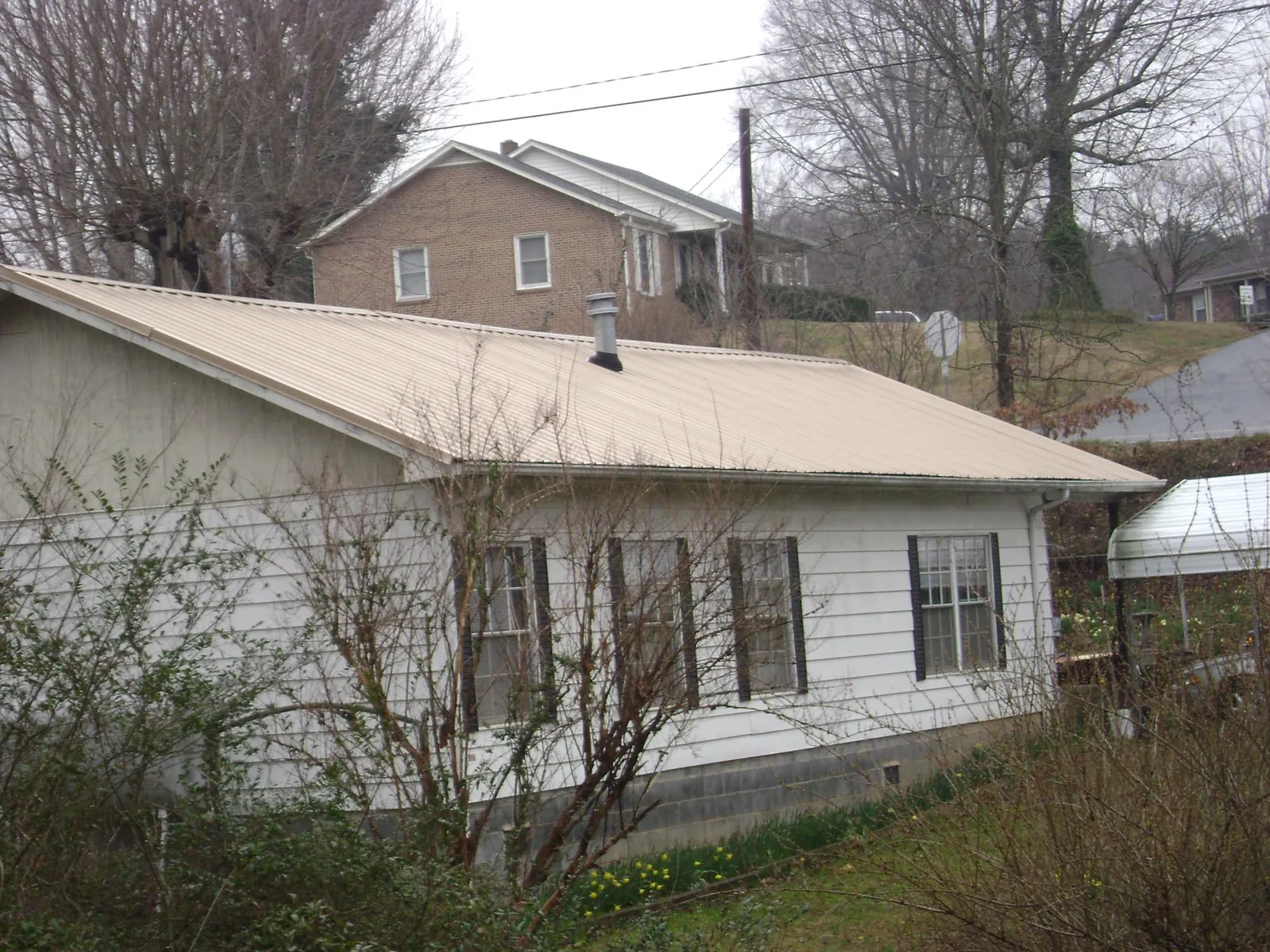 Tan metal roof on a white sided house set into a hillside — Commercial Roofing by Roofing Brothers in Potrero